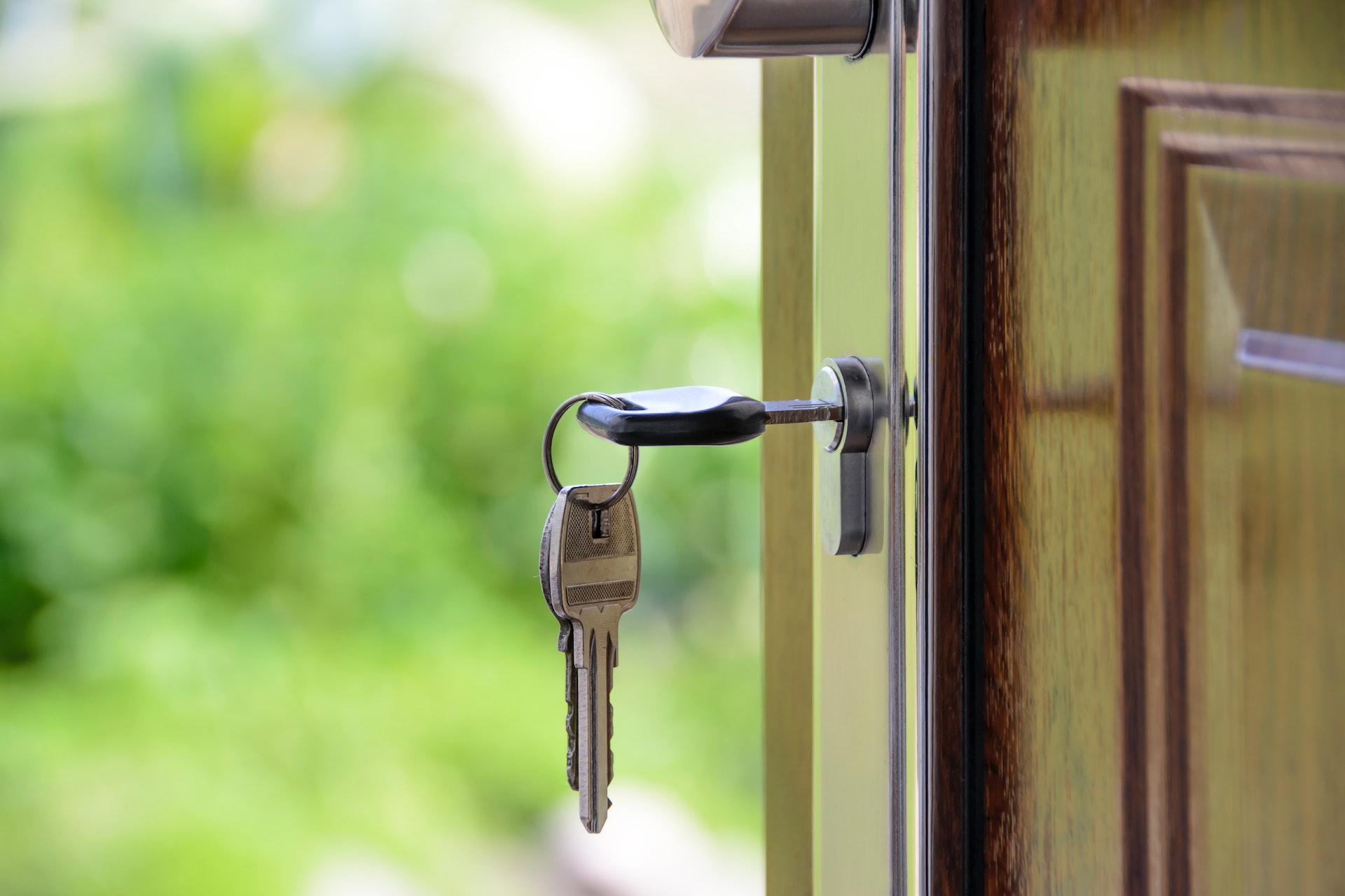 A door with a key in the lock. The door is open and shows green bushes and trees outside